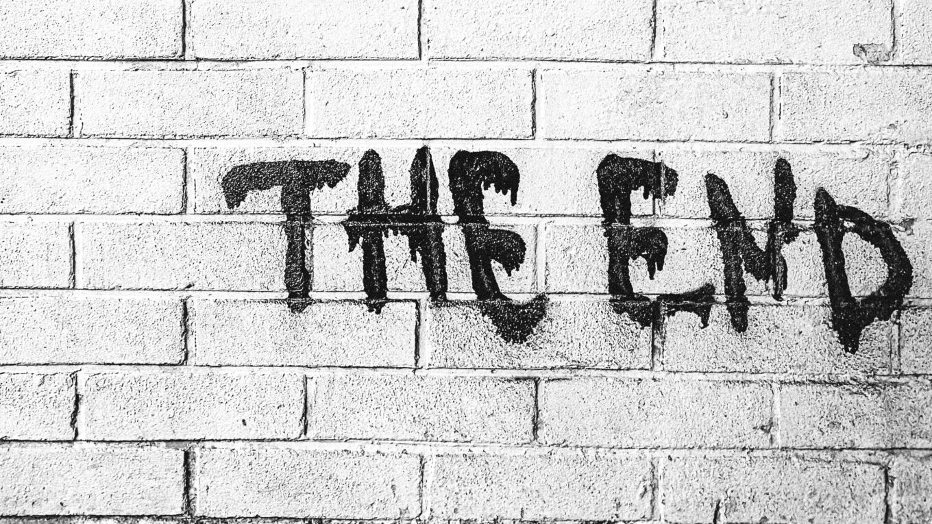 black spray painted on a brick wall, words saying The End